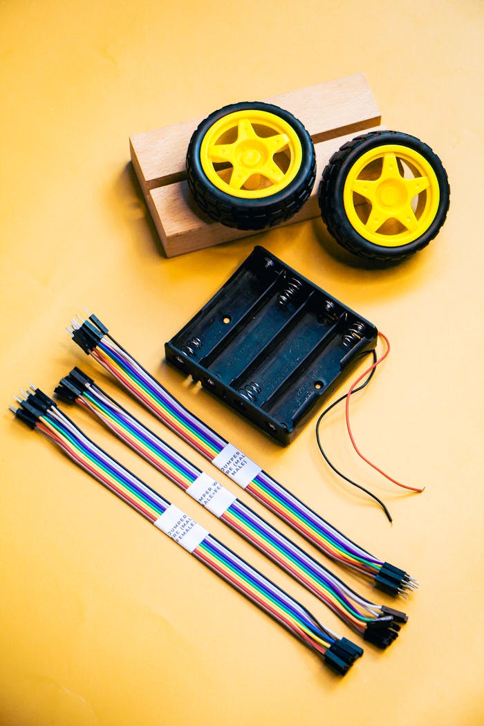 Robotics kit with wheels, wires, and battery holder on a yellow surface.